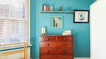 A room with teal walls, a wooden dresser with drawers, a shelf with books and a small statue, a framed picture, and a window with blinds.