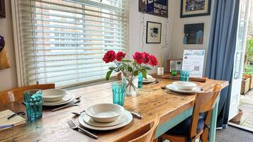 Une table à manger dressée avec des assiettes, des couverts et des verres bleus, et un vase rempli de fleurs rouges placé au centre.