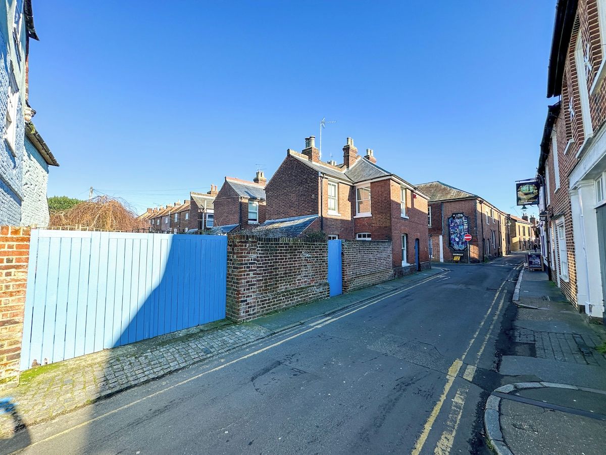 Une rue étroite bordée de maisons en briques, avec une porte bleue et une enseigne de pub.
