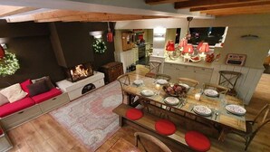 A cozy dining area with a wooden table set for six, surrounded by wooden chairs with red cushions. A fireplace is visible in the background, and a kitchen area is adjacent to the dining space. - Chalet, wifi, 130m from resort center, sauna, terrace, parking, tv, ski locker, 450m², Alpe d'Huez (L'Alpe d'Huez)