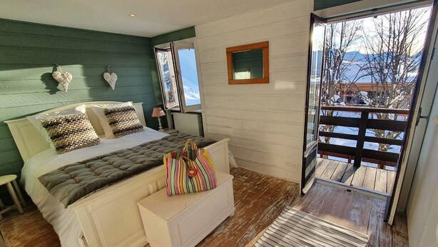 A bedroom with a bed, bedside table, and a view of a snowy landscape through a sliding door. - Chalet, wifi, 130m from resort center, sauna, terrace, parking, tv, ski locker, 450m², Alpe d'Huez (L'Alpe d'Huez)