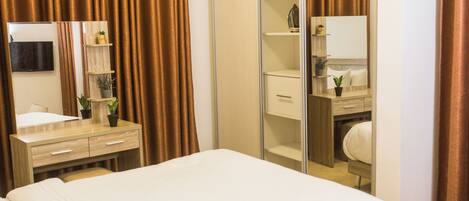A hotel room with a bed, a desk with a mirror, a wardrobe, and a television on the wall.