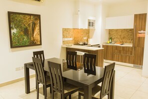 A modern kitchen with a dining area, featuring a tiled backsplash, wooden cabinets, and a large framed picture on the wall. - Accra Luxury Apartments at Avant Garde (Accra)