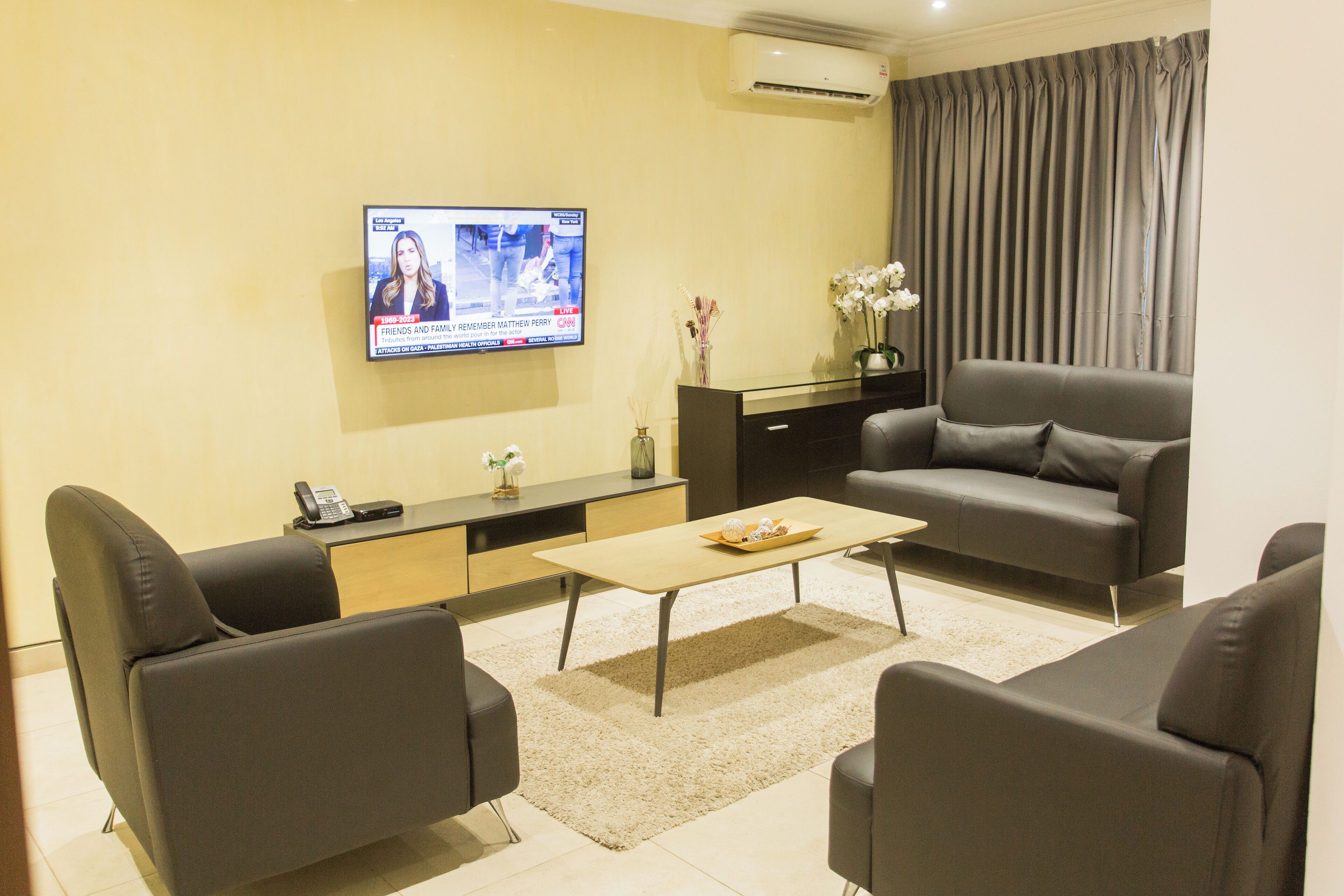 A modern living room with a flat-screen TV, a sofa, a coffee table, and a desk with a phone.
