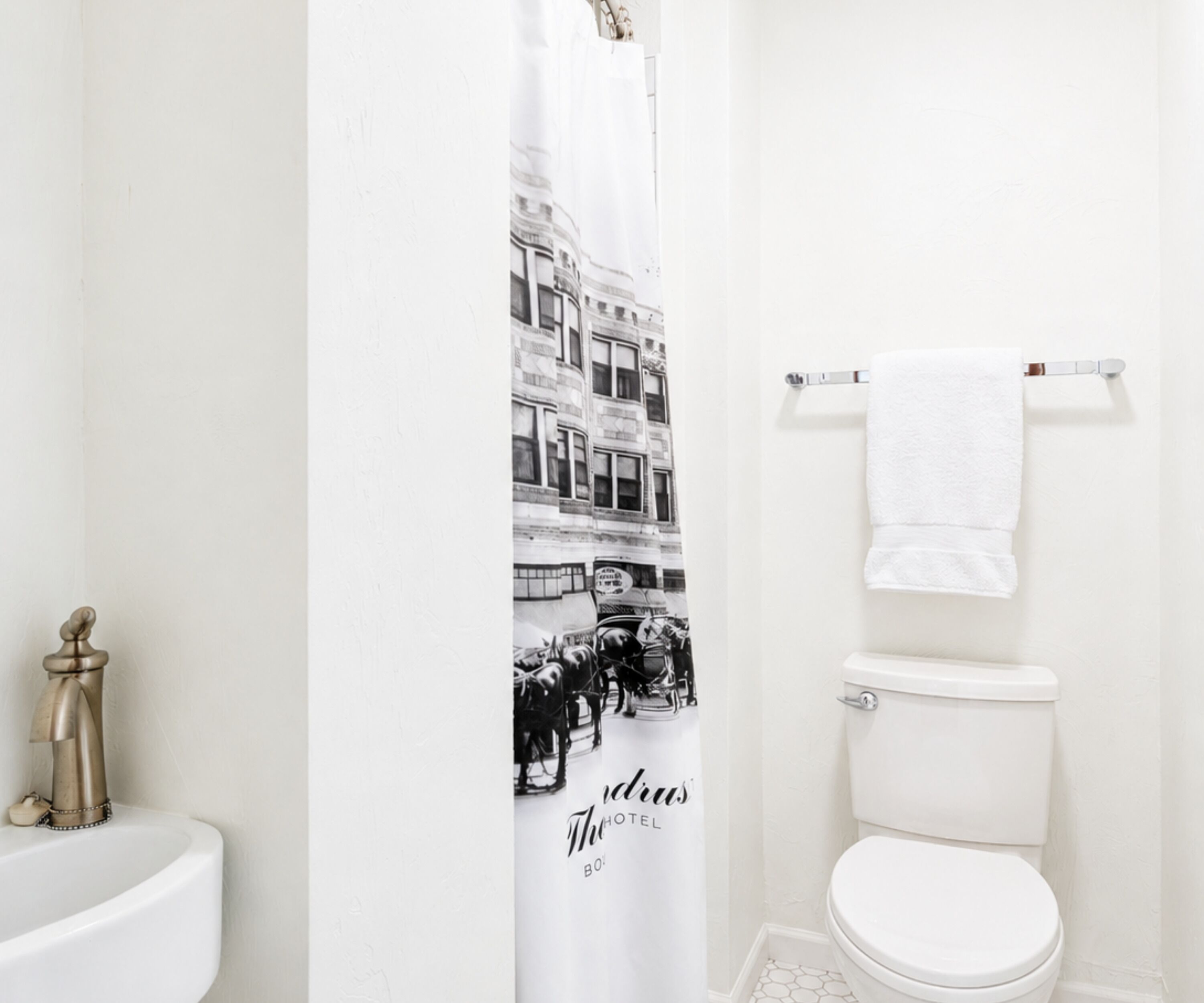 A bathroom with a white sink, a toilet, and a shower curtain with a black and white photo of a street scene.