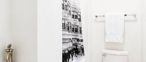 A bathroom with a white sink, a toilet, and a shower curtain with a black and white photo of a street scene.