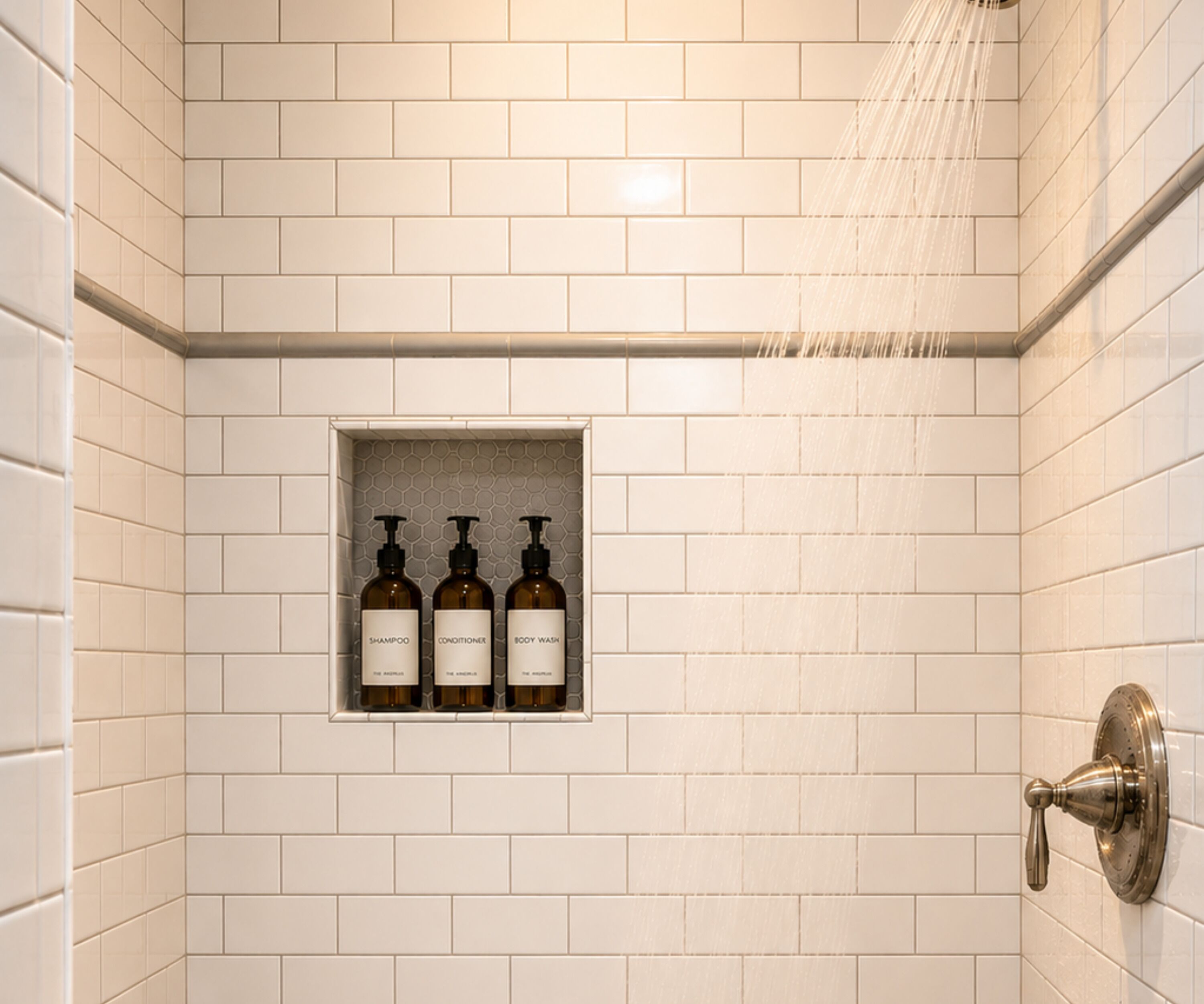 En bruser med en vægmonteret hylde, der indeholder tre flasker mærket 'SHAMPOO', 'CONDITIONER' og 'BODY WASH'.