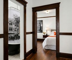 Una habitación de hotel con cama, mesita de noche, lámpara y vista a la calle a través de una ventana.