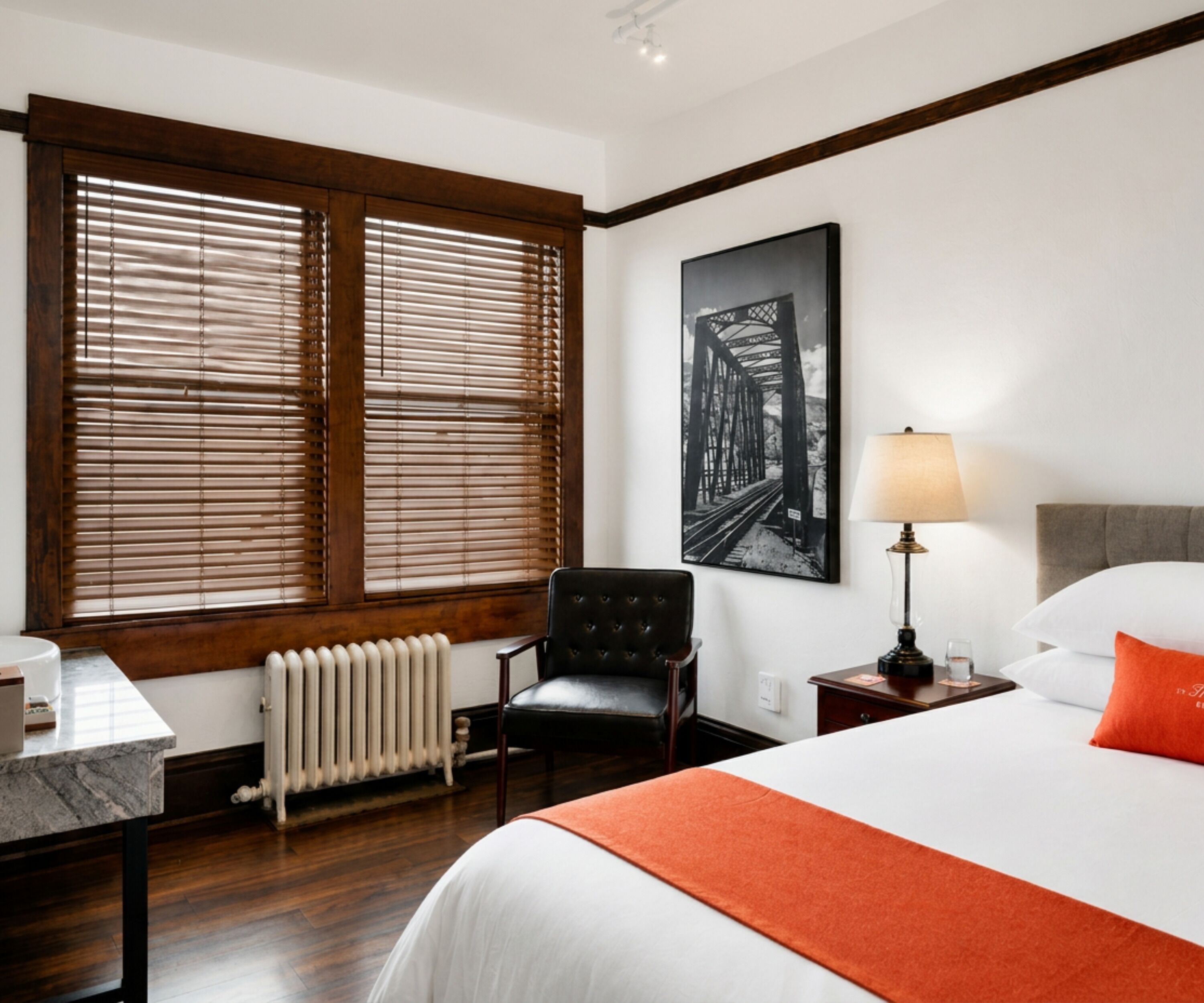 Una habitación de hotel con cama, una silla, un escritorio, una lámpara y una ventana con persianas.