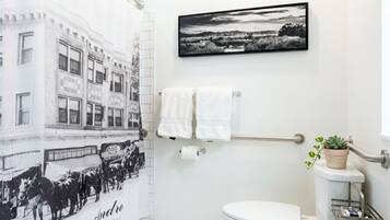 Une salle de bain avec un rideau de douche orné d’un motif représentant un bâtiment ancien, des toilettes, un porte-serviettes et un tableau représentant un paysage, encadré.