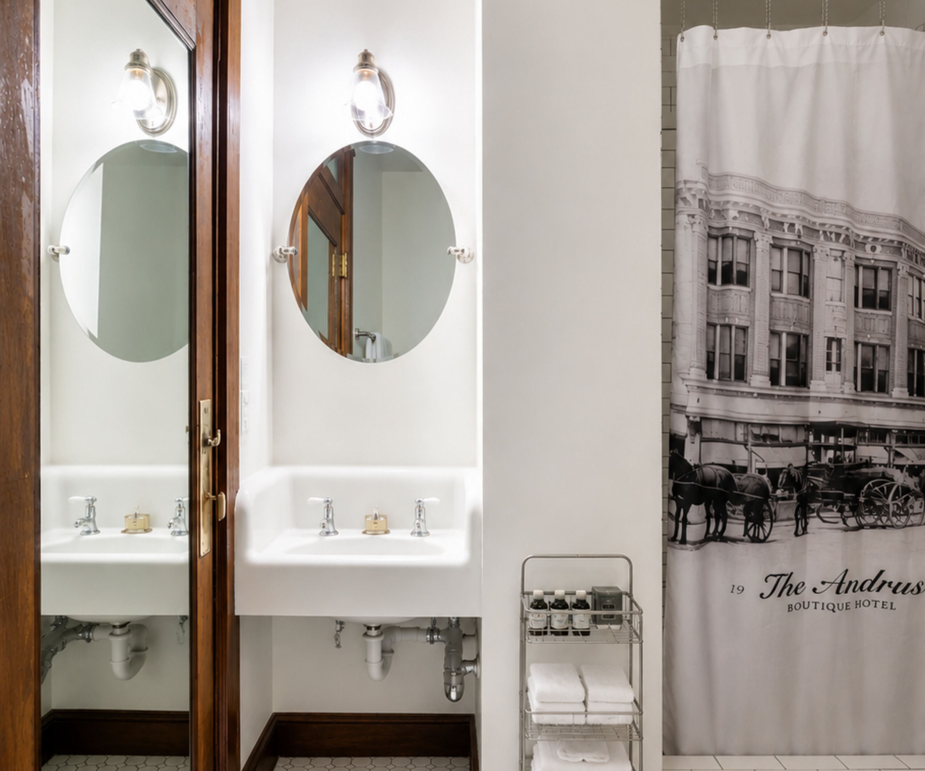 A bathroom with two sinks, a mirror, a towel rack, and a poster of a building.