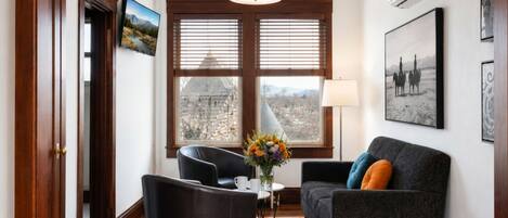 A room with a sofa, a chair, a table with a vase, a lamp, and a window with blinds.