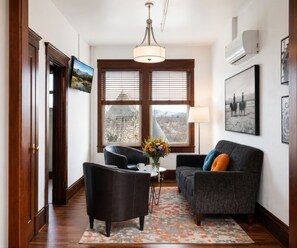 A room with a sofa, a chair, a table with a vase, a lamp, and a window with blinds. - The Andrus Hotel (Dillon)