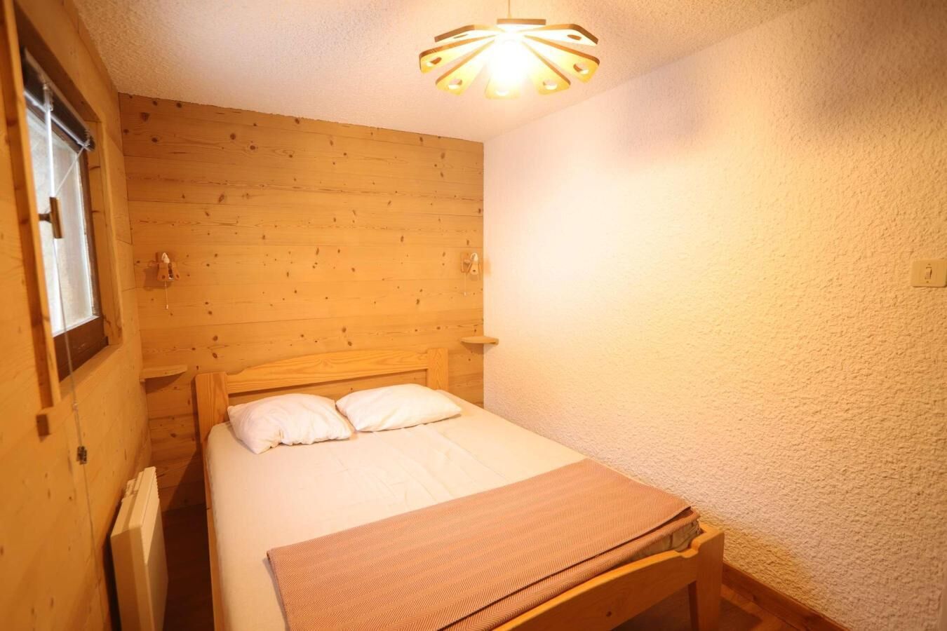 Una habitación pequeña y acogedora con cama de cabecera de madera, una mesita de noche individual y una lámpara de techo original.