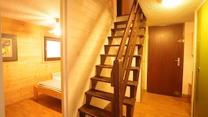 Una scala in legno conduce a un secondo piano, un letto in una stanza con pareti di legno e una porta alla destra.