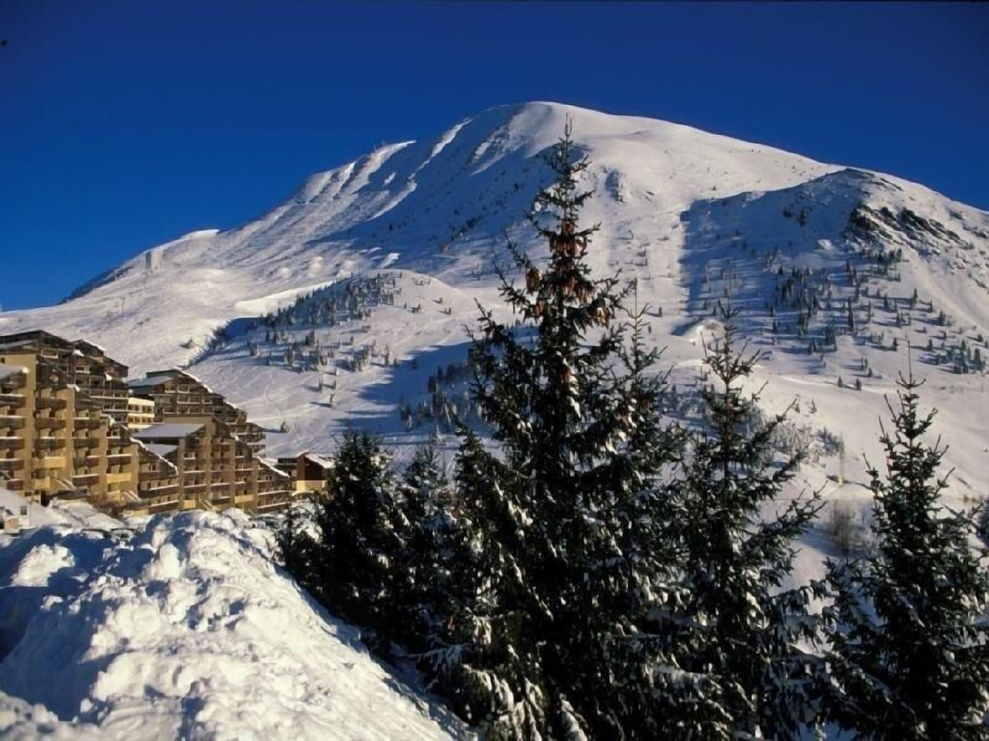 A snow-covered mountain with a ski resort in the foreground, including buildings and trees.