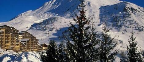 A snow-covered mountain with a ski resort in the foreground, including buildings and trees.