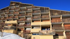 Un hotel a più piani con balconi, terreno innevato e cielo azzurro limpido.