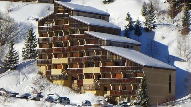 Un hotel a più piani con balconi, immerso in un paesaggio innevato tra alberi.