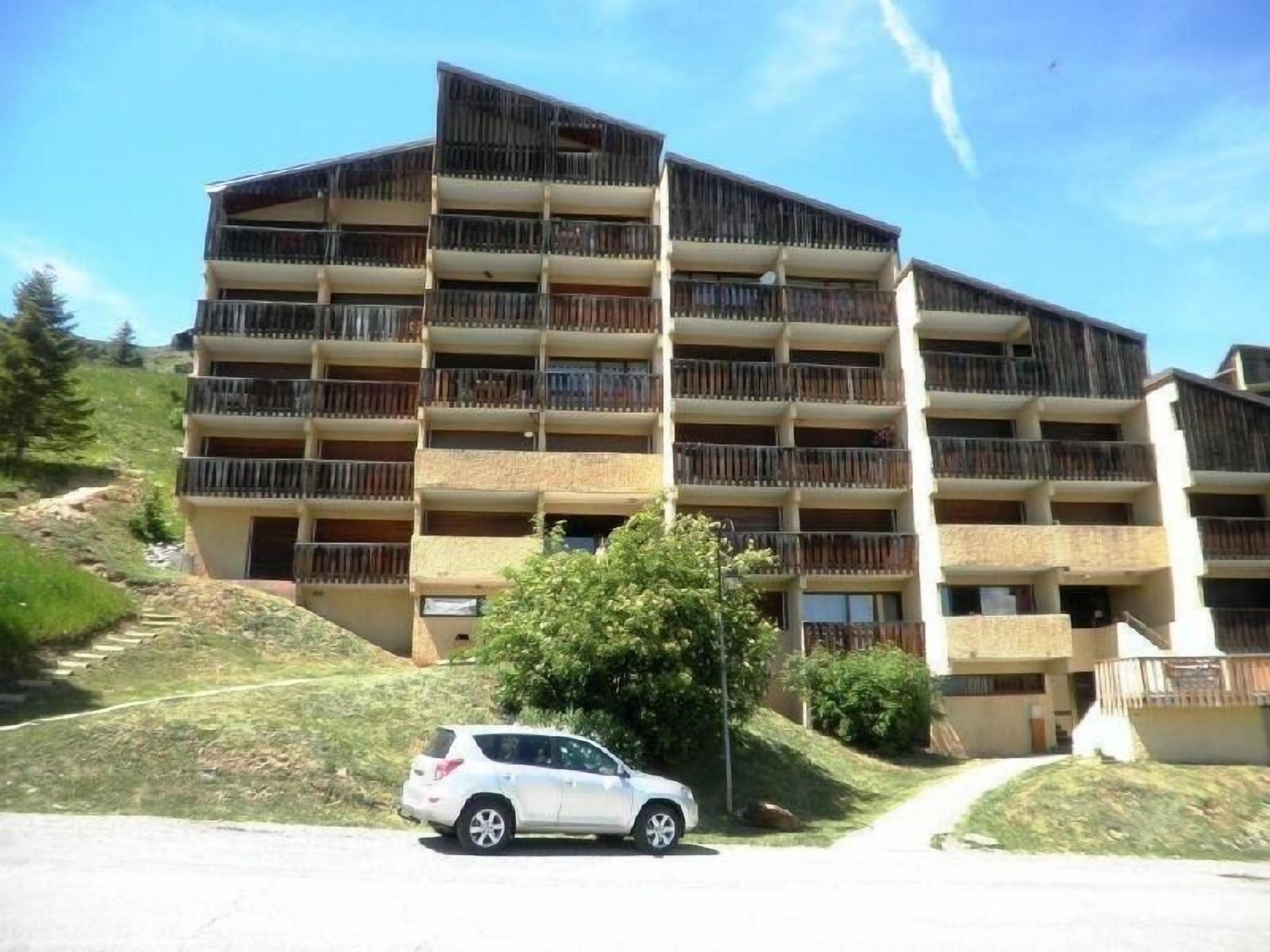 A multi-story building with balconies, a parking area, and a pathway leading up to it.