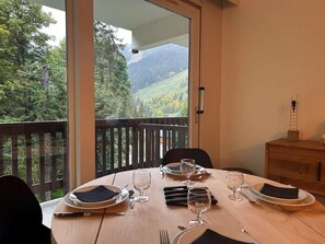 Une table à manger dressée pour quatre personnes, avec vue sur une colline boisée.