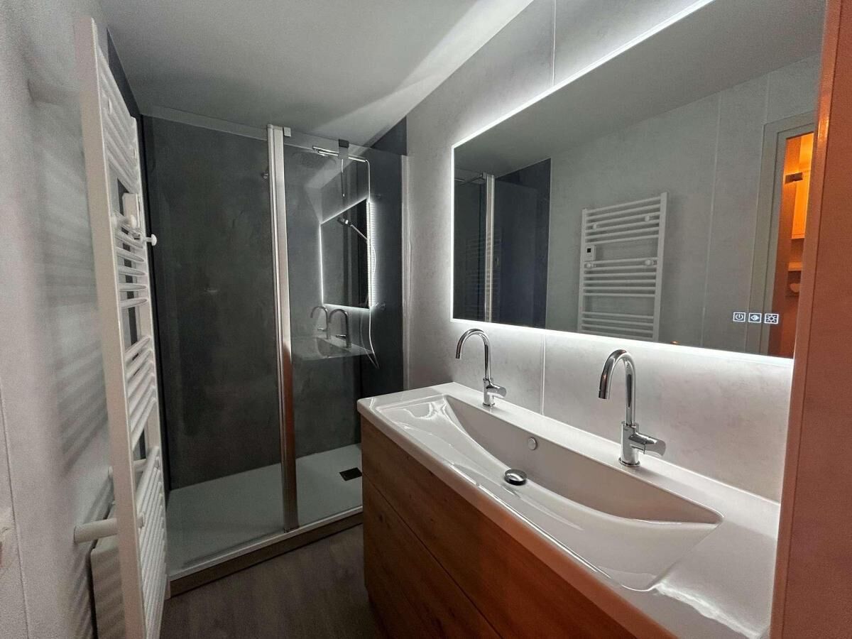 Uma casa de banho moderna com cabine de duche, um espelho grande e uma toucador com lavatório.