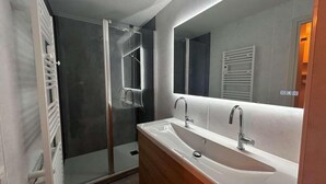 Ein modernes Badezimmer mit begehbarer Dusche, einem großen Spiegel und einem Waschtisch.