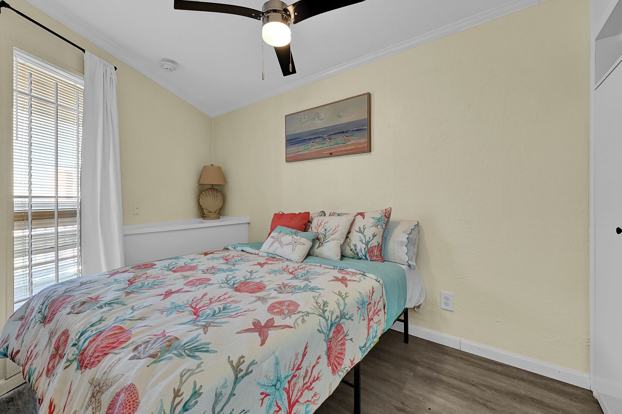 A bedroom with a bed, a ceiling fan, a painting, and a window with blinds.