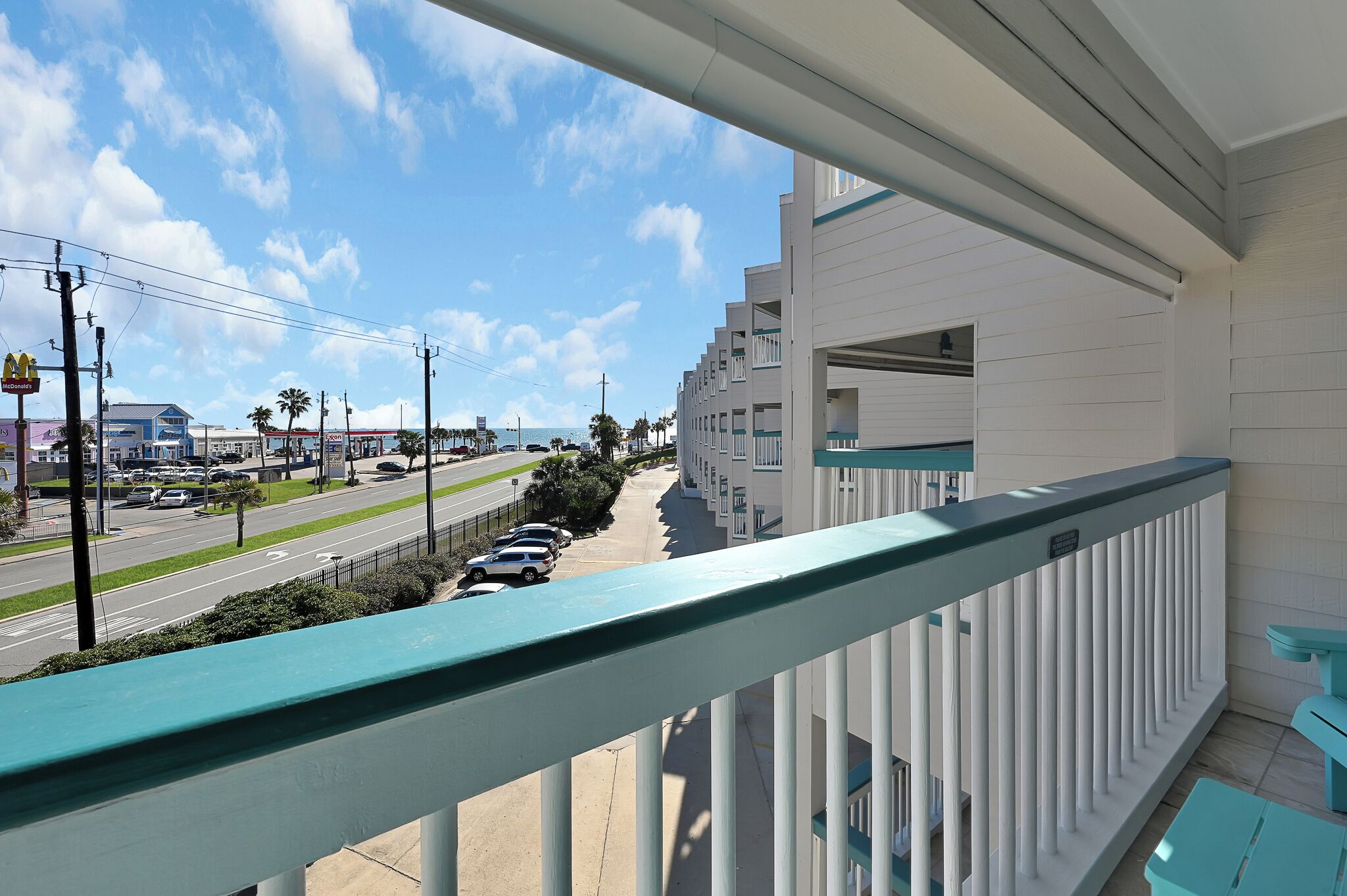 A balcony with a view of a street, a parking lot, and a building with a white facade and balconies.