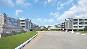 Et hotel med et skilt, der viser "Casa del Mar Suites and Rentals". Det fremstår som en stor, moderne bygning med flere altaner og en velplejet græsplæne.