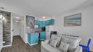 En moderne stue med en grå sofa, et køkken med blå skabe og et maleri på væggen.