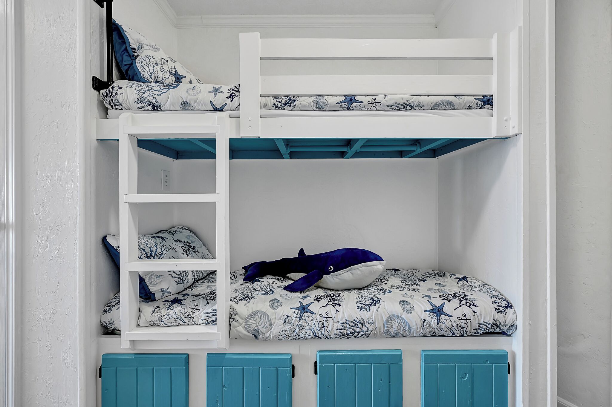 Un lit superposé avec une échelle, un gros jouet en forme de baleine et une couverture à motifs.