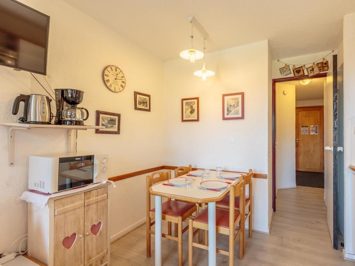 A cozy kitchen with a dining table, chairs, a microwave, a kettle, and a clock on the wall.