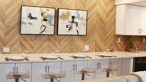 Eine moderne Küche mit Wandpaneelen in Fischgrätmuster, zwei abstrakte Gemälde, einer Bar mit Hockern und weißen Schränken.