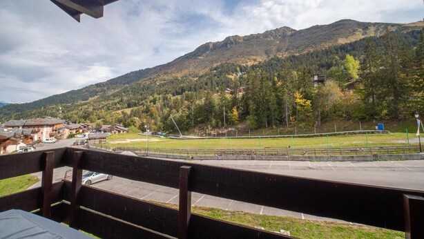 On peut admirer une vue sur les montagnes depuis une terrasse en bois qui surplombe une ville avec ses bâtiments et une route.