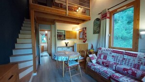 A cozy interior with a wooden staircase, a dining area with a round table, and a sofa with a patterned cover. - 50m from ski slopes, 11st floor, balcony, ski locker, 45m², Valmorel (Valmorel)