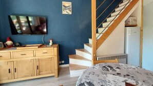 A bedroom with a bed, a wooden dresser, a television, a staircase, and a small shelf with items. - 50m from ski slopes, 11st floor, balcony, ski locker, 45m², Valmorel (Valmorel)
