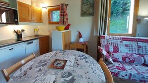 A cozy kitchen with wooden cabinets, a microwave, and a sink. There's a table with a book and a patterned tablecloth. A window with curtains and a view of greenery is visible. - 50m from ski slopes, 11st floor, balcony, ski locker, 45m², Valmorel (Valmorel)