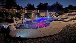 A swimming pool with a circular light pattern, surrounded by lounge chairs and a stone deck. - Spacious 5-bedroom house with Heated Pool, hot tub and fire pit. (Goodyear)