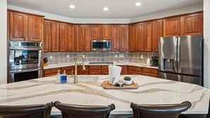 A kitchen with wooden cabinets, stainless steel appliances, and a marble island. - Spacious 5-bedroom house with Heated Pool, hot tub and fire pit. (Goodyear)