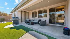 An outdoor patio with a grill, seating area, and sliding glass doors. - Spacious 5-bedroom house with Heated Pool, hot tub and fire pit. (Goodyear)