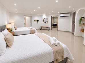 A hotel room with two beds, a bench, a mirror, and an air conditioning unit.