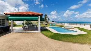 Un patio trasero con piscina, un porche cubierto y vista al océano.