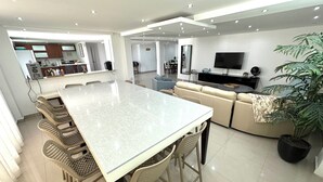 Una cocina moderna con una isla central, un área de comedor con sillas, un sofá y un televisor.