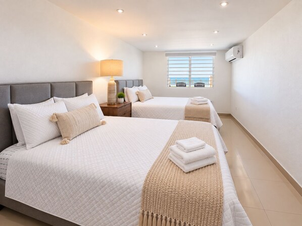 A hotel room with two beds, a nightstand, a lamp, and a window with a view. - Breathtaking Beachfront Gem in Luquillo – Walk to Kiosks & Hidden Bars (Playa Fortuna)