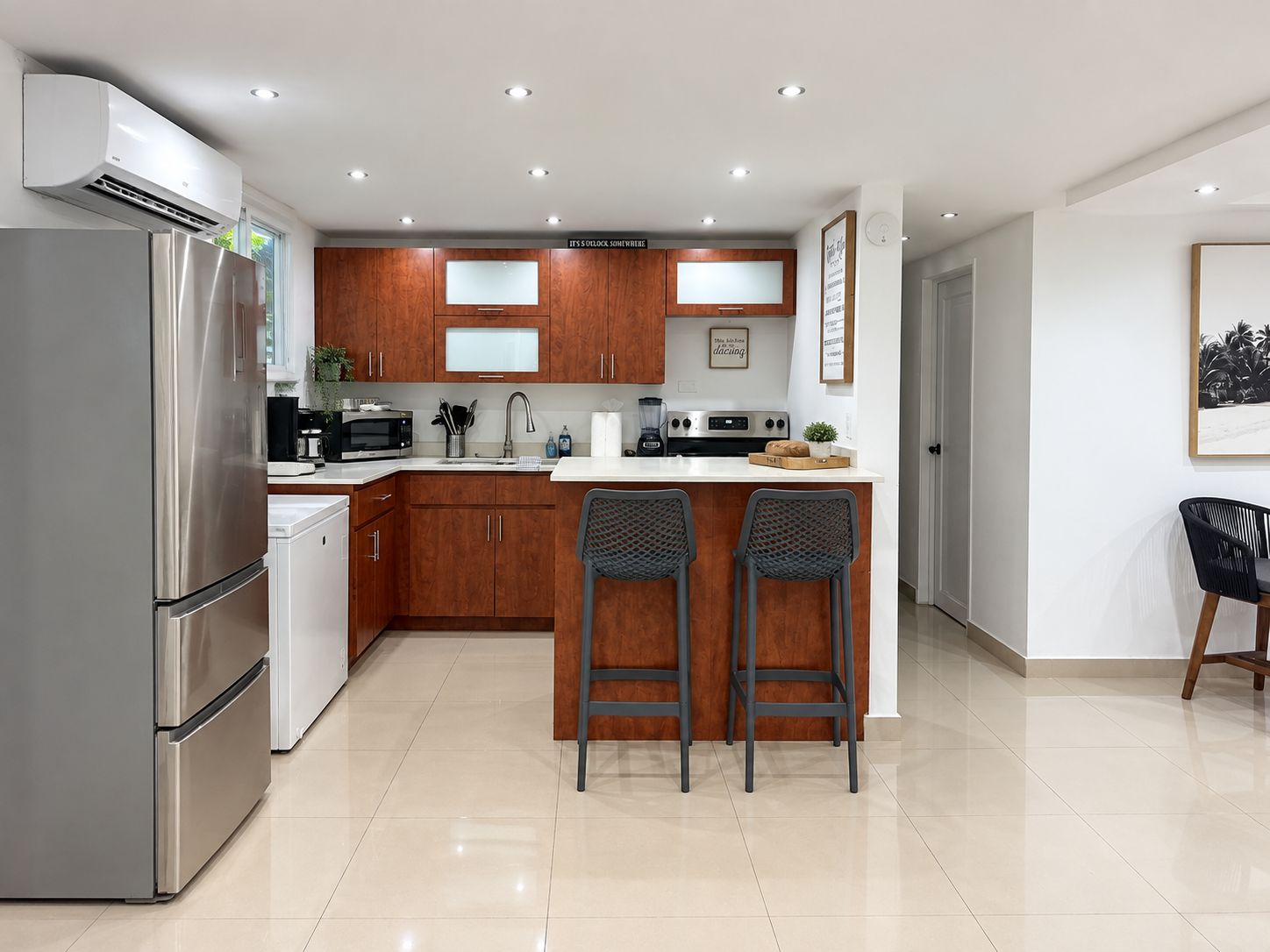 A modern kitchen with stainless steel appliances, wooden cabinets, and a bar area with two stools.
