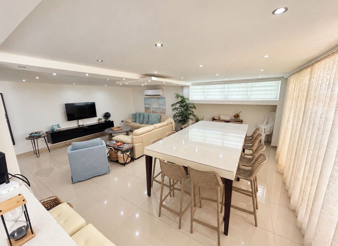 A modern living room with a dining area, a flat-screen TV, and a large window with curtains.
