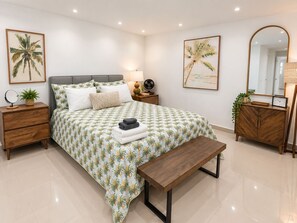 A bedroom with a bed, bedside tables, a bench, a dresser, and a mirror.
