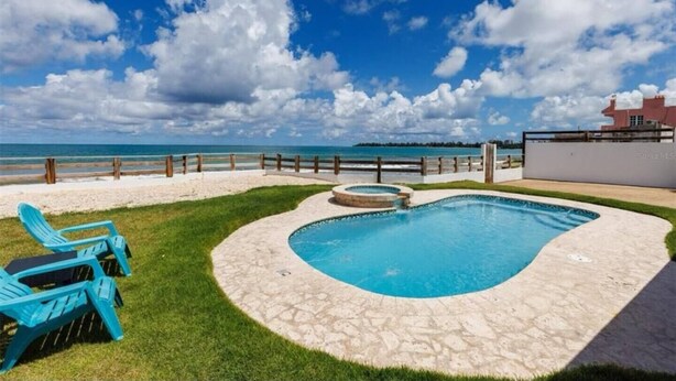 Una piscina de diseño curvo, rodeada por una terraza de piedra y un césped con sillas azules.
