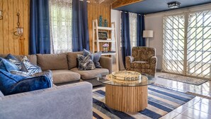 Un salon chaleureux avec un canapé, un fauteuil et une table basse, des murs en bois et une grande fenêtre avec des rideaux.